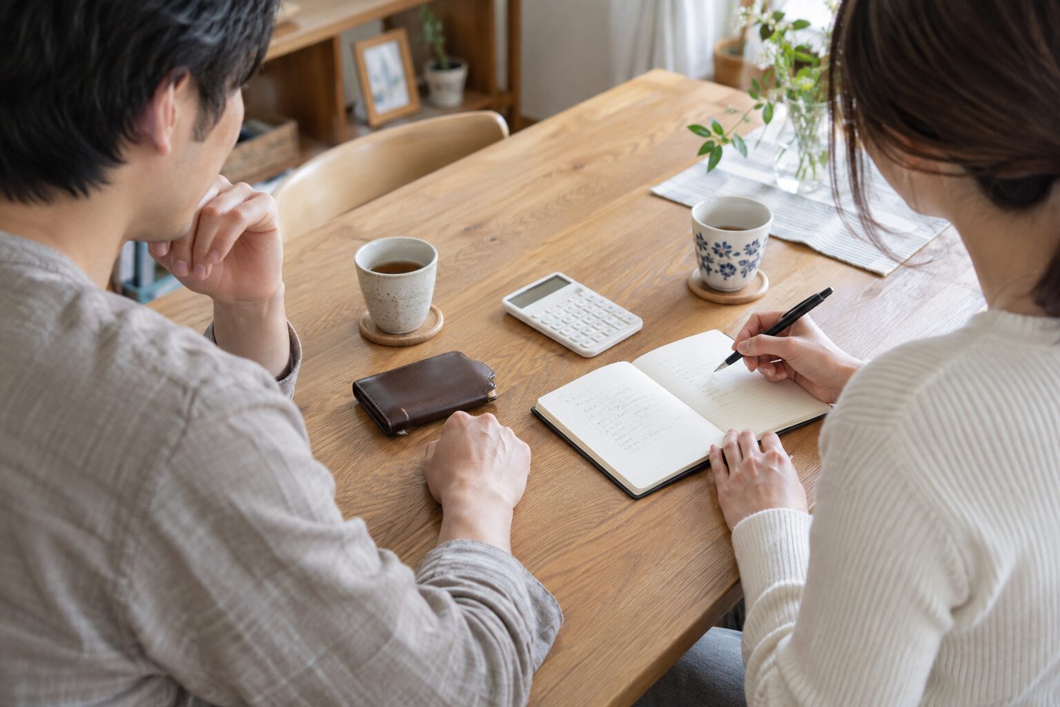 ノートと電卓を置いたテーブルでデートの予算を相談する二人の手元