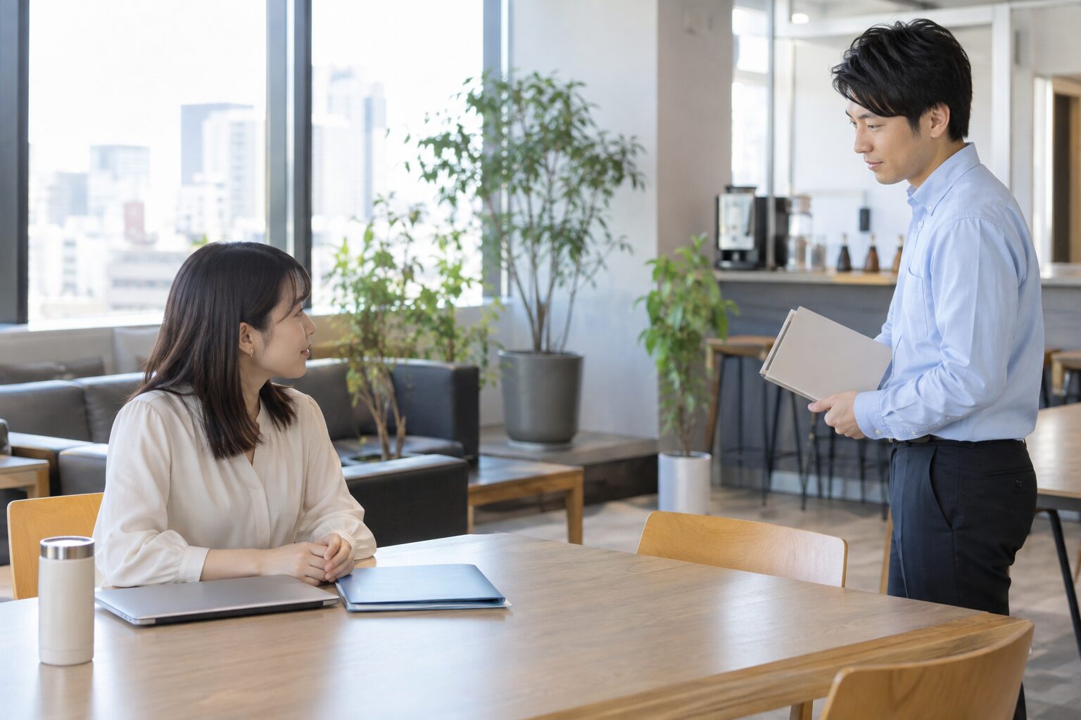 職場の共有スペースで距離を保ちながら業務のやり取りをする二人