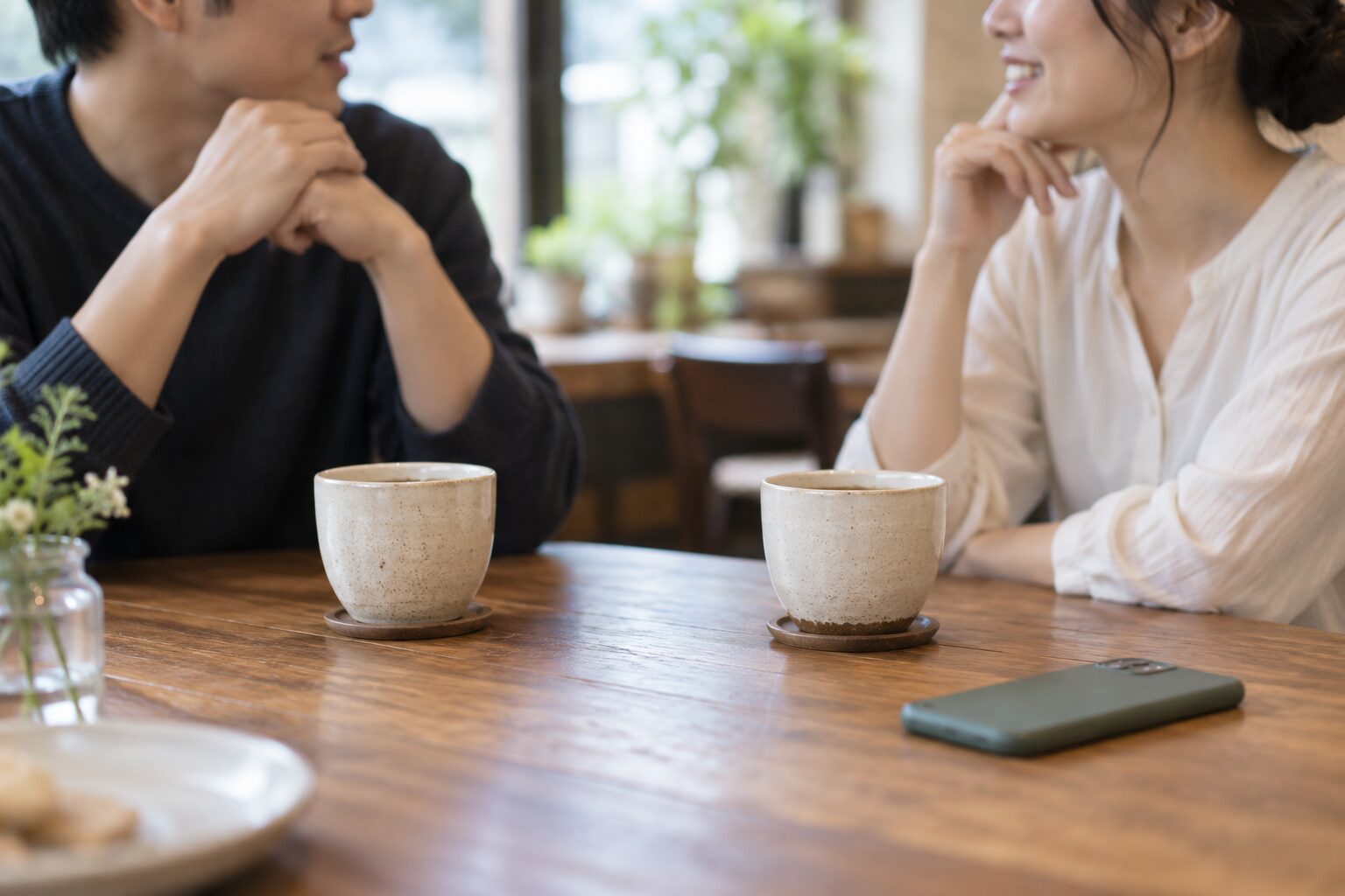 スマートフォンを脇に置いてカフェで会話する恋人たち